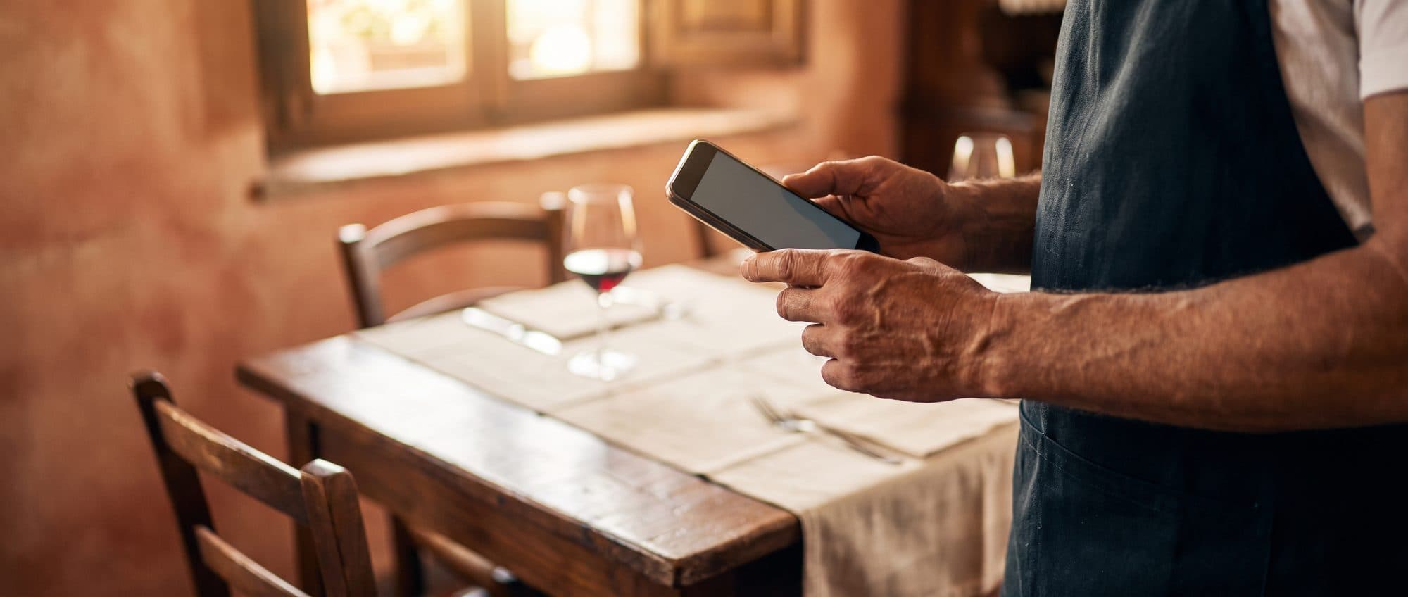 Cameriere in una trattoria che tiene in mano uno smartphone accanto a un tavolo apparecchiato